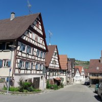 Fachwerkhäuser in Rosswag unter klarem, blauem Himmel. Die Straße ist gesäumt von geparkten Autos und traditionellen Gebäuden., © Land der 1000 Hügel - Kraichgau-Stromberg Fachwerkhäuser in Rosswag unter klarem, blauem Himmel. Die Straße ist gesäumt von geparkten Autos und traditionellen Gebäuden., © Land der 1000 Hügel - Kraichgau-Stromberg