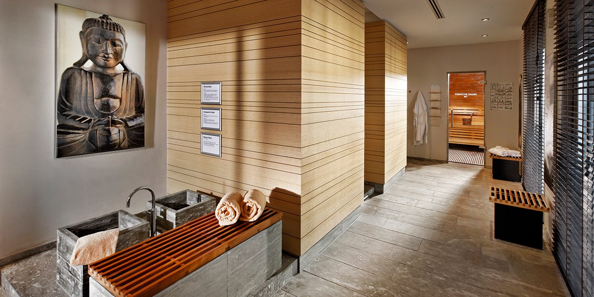 Ein Spa-Bereich mit Buddha-Bild, Holzverkleidung, Handtüchern und einer Sauna im Hintergrund., © Parkhotel Stuttgart Messe-Airport
