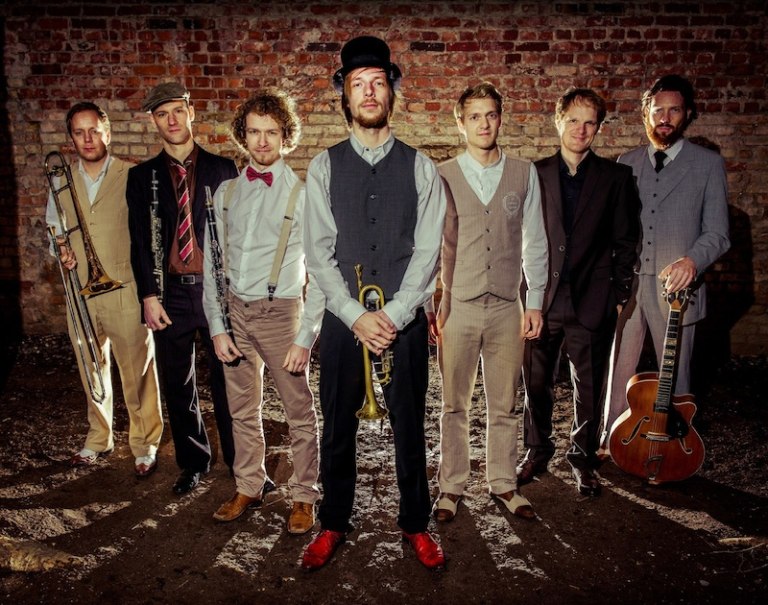 Eine Jazzband in Vintage-Kleidung posiert vor einer Backsteinwand. Die Mitglieder halten Instrumente wie Trompete und Gitarre und blicken in die Kamera., &copy; Stadt B&ouml;blingen - Amt f&uuml;r Kultur