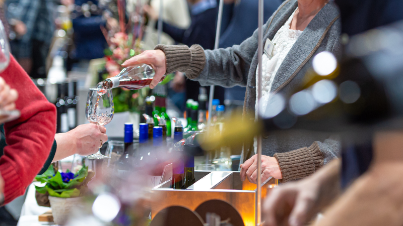 Eine Person schenkt bei einer Weinverkostung Ros&eacute;wein in ein Glas ein. Im Hintergrund sind weitere Flaschen und Besucher zu sehen., &copy; Peter Schuster