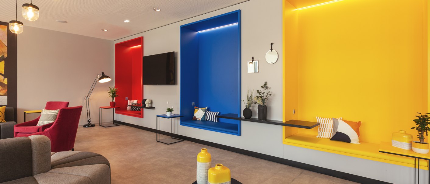Moderne Lobby mit bunten Sitznischen in Rot, Blau und Gelb, dekoriert mit Kissen und Pflanzen., © the niu Form - Novum Hospitality
