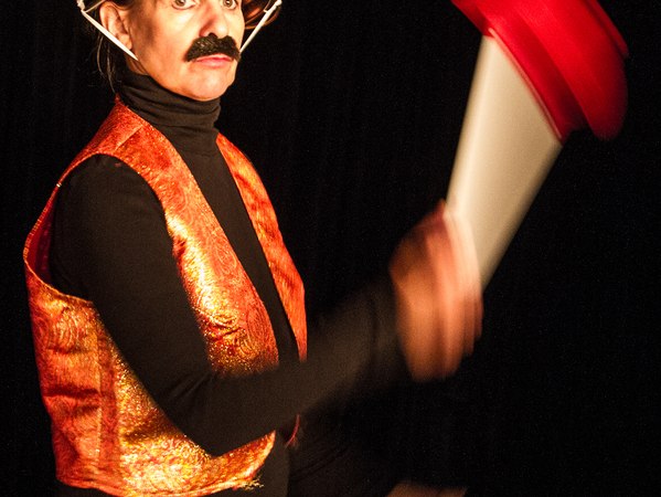 Eine Person in einem kreativen Theaterkost&uuml;m mit einem Sieb als Helm und einem roten Requisit in der Hand, vor schwarzem Hintergrund., &copy; Galli Theater Backnang