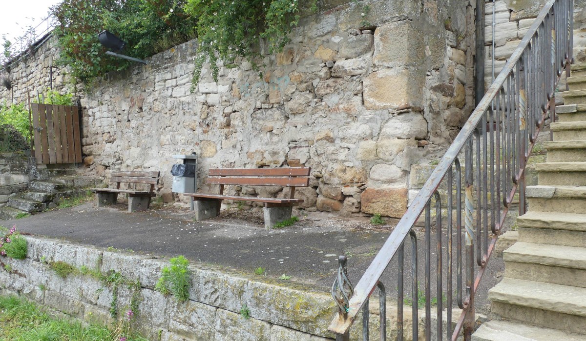 Steinmauer mit zwei Holzbänken und einer Treppe. Die Mauer ist von Pflanzen umgeben, und es gibt einen Mülleimer zwischen den Bänken., © Stadt Sachsenheim Steinmauer mit zwei Holzbänken und einer Treppe. Die Mauer ist von Pflanzen umgeben, und es gibt einen Mülleimer zwischen den Bänken., © Stadt Sachsenheim