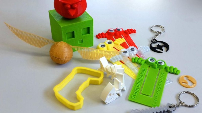 Bunte 3D-gedruckte Objekte auf einem Tisch, darunter ein roter Vogel, ein gr&uuml;ner W&uuml;rfel, Lineale mit Augen und verschiedene Schl&uuml;sselanh&auml;nger., &copy; Stadtbibliothek Ludwigsburg