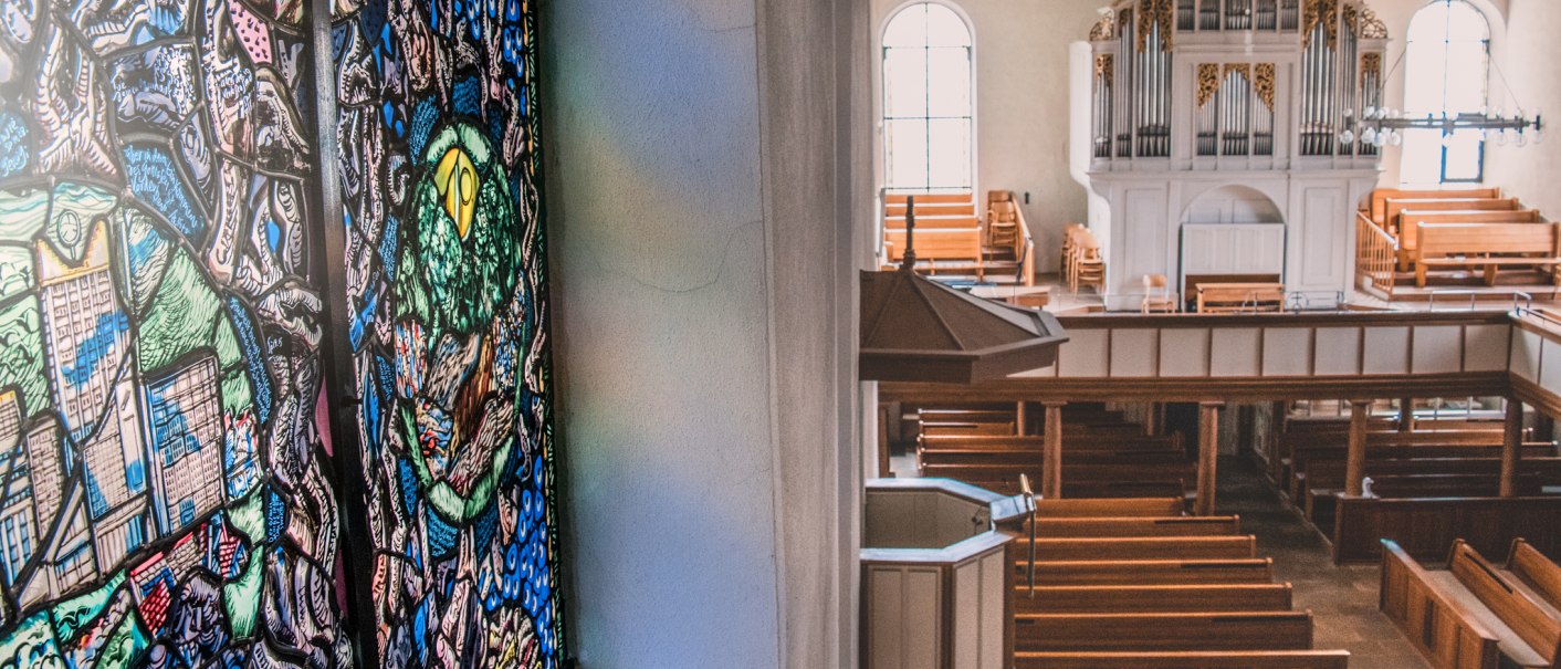 Buntes Glasfenster in einer Kirche, das Licht auf die Wand wirft. Im Hintergrund eine große Orgel und Holzbänke., © Stadt Welzheim Buntes Glasfenster in einer Kirche, das Licht auf die Wand wirft. Im Hintergrund eine große Orgel und Holzbänke., © Stadt Welzheim