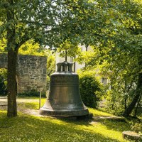 Eine große Glocke steht im Garten der Stiftskirche Herrenberg, umgeben von Bäumen und einer alten Steinmauer. Sonnenlicht fällt durch das Blätterdach., © Stuttgart-Marketing GmbH, Sarah Schmid Eine große Glocke steht im Garten der Stiftskirche Herrenberg, umgeben von Bäumen und einer alten Steinmauer. Sonnenlicht fällt durch das Blätterdach., © Stuttgart-Marketing GmbH, Sarah Schmid