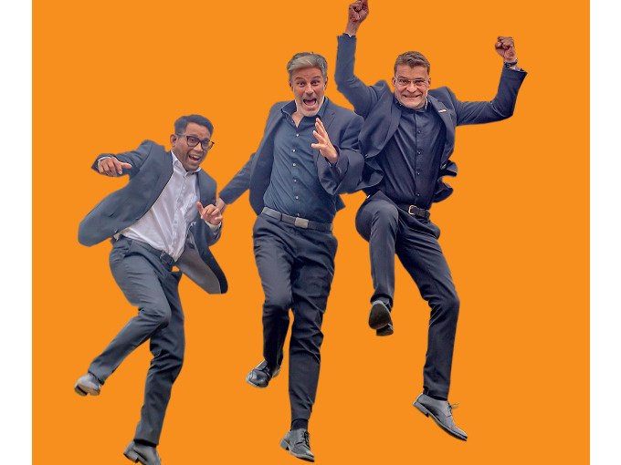 Drei Männer in Anzügen springen fröhlich in die Luft vor einem orangefarbenen Hintergrund. Sie wirken energiegeladen und begeistert., © Stadt Murrhardt Drei Männer in Anzügen springen fröhlich in die Luft vor einem orangefarbenen Hintergrund. Sie wirken energiegeladen und begeistert., © Stadt Murrhardt