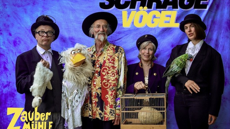 Vier Personen in bunten Kostümen posieren mit Vögeln und Puppen vor einem blauen Hintergrund. Schriftzug: Schräge Vögel, Zaubermühle Merklingen., © Zaubermühle Merklingen Vier Personen in bunten Kostümen posieren mit Vögeln und Puppen vor einem blauen Hintergrund. Schriftzug: Schräge Vögel, Zaubermühle Merklingen., © Zaubermühle Merklingen