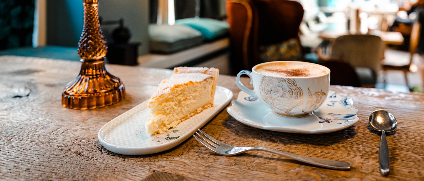 Ein St&uuml;ck Kuchen und eine Tasse Kaffee auf einem Holztisch in einem gem&uuml;tlichen Caf&eacute;. Im Hintergrund unscharfe M&ouml;bel., &copy; Stuttgart-Marketing GmbH, Sarah Schmid