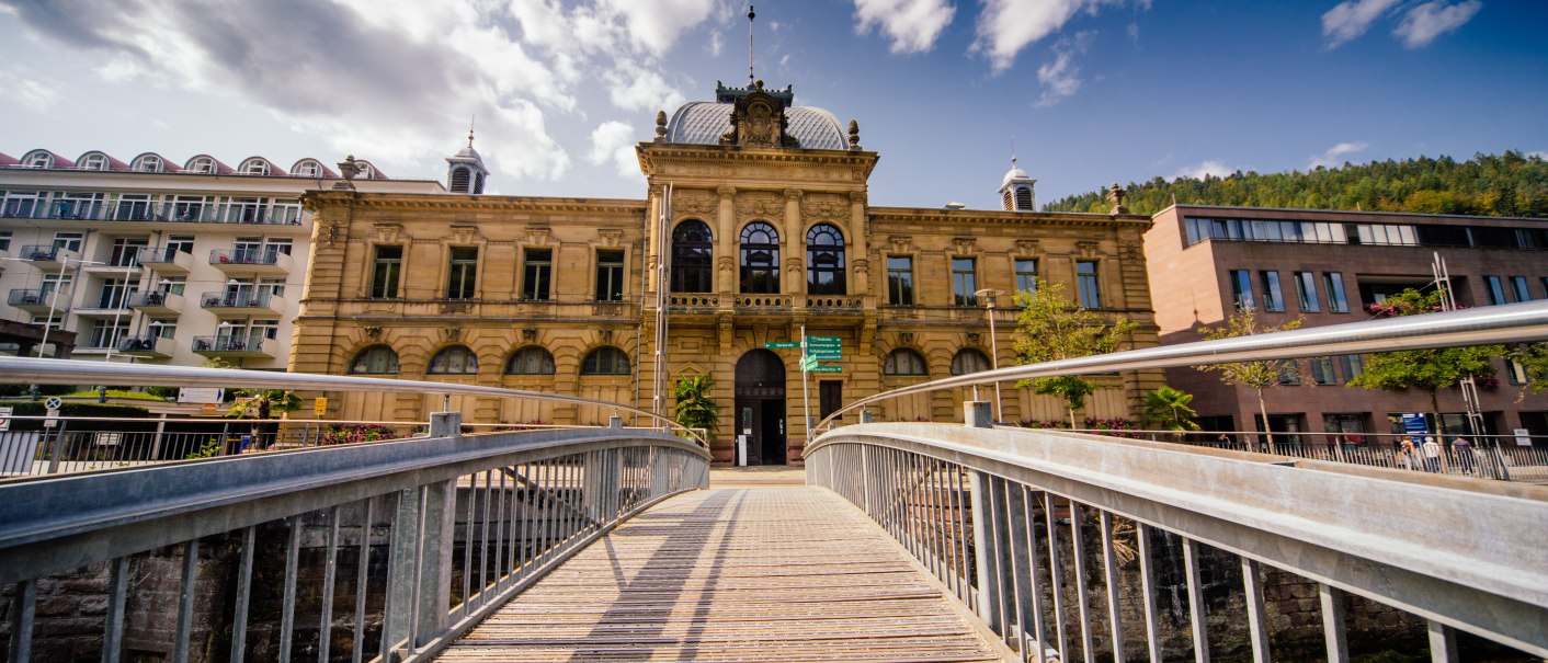 Historisches Gebäude in Bad Wildbad, Deutschland, mit einer Holzbrücke im Vordergrund und blauem Himmel im Hintergrund., © Touristik Bad Wildbad Historisches Gebäude in Bad Wildbad, Deutschland, mit einer Holzbrücke im Vordergrund und blauem Himmel im Hintergrund., © Touristik Bad Wildbad