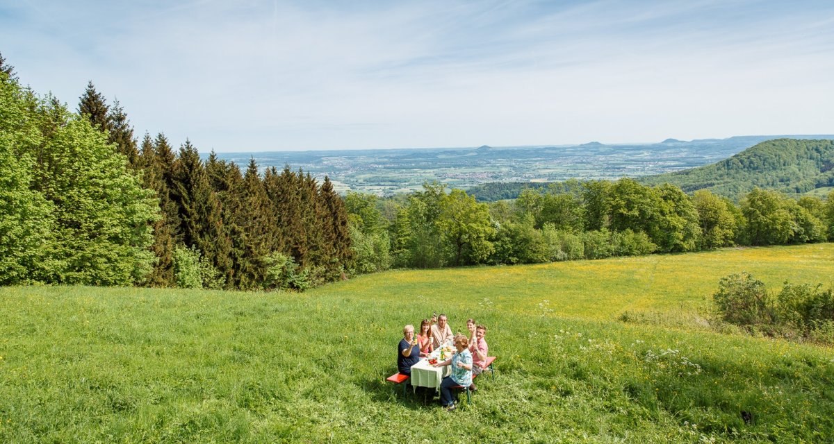 Eine Gruppe von Menschen sitzt an einem Tisch auf einer gr&uuml;nen Wiese. Im Hintergrund sind die Drei Kaiserberge und eine weite Landschaft zu sehen., &copy; Landkreis G&ouml;ppingen