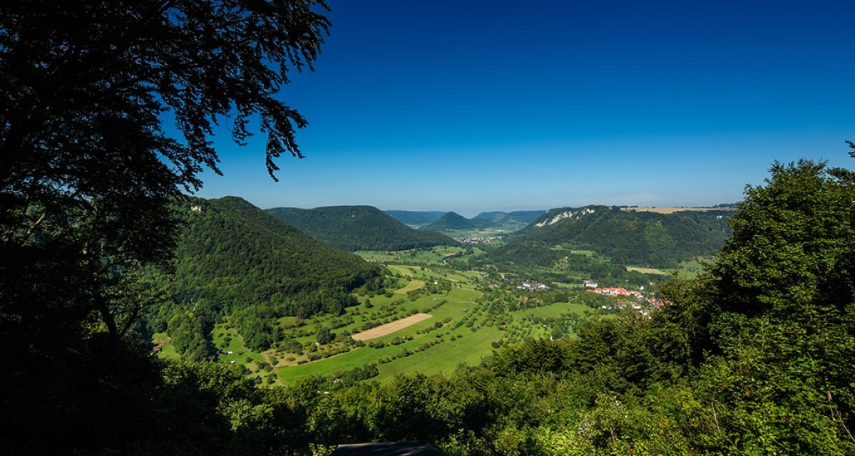 Panoramablick ins grüne Filstal bei Bad Überkingen, umgeben von bewaldeten Hügeln und unter klarem, blauem Himmel., © Distretto di Göppingen Panoramablick ins grüne Filstal bei Bad Überkingen, umgeben von bewaldeten Hügeln und unter klarem, blauem Himmel., © Distretto di Göppingen
