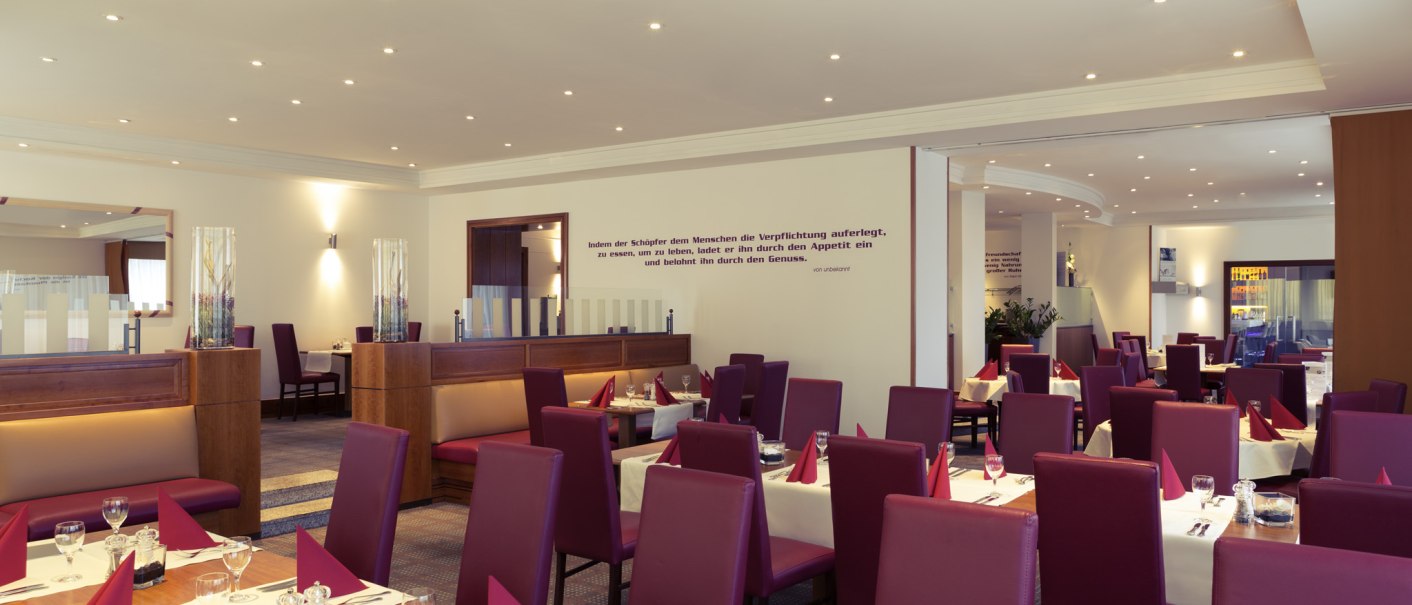 Elegantes Restaurant mit roten Stühlen, gedeckten Tischen und moderner Beleuchtung. An der Wand ein Zitat über Essen und Genuss., © Mercure Bristol Stuttgart Sindelfingen