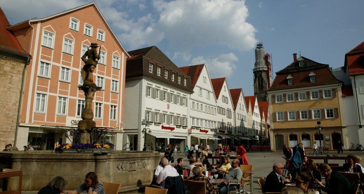 Der Reutlinger Marktplatz mit Menschen, die an Tischen sitzen. Historische Gebäude und ein Brunnen sind im Hintergrund zu sehen., © Sphäre Verlag Der Reutlinger Marktplatz mit Menschen, die an Tischen sitzen. Historische Gebäude und ein Brunnen sind im Hintergrund zu sehen., © Sphäre Verlag