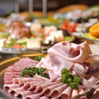 Ein Teller mit verschiedenen Wurstsorten, darunter Schinken und Salami, dekoriert mit Petersilie. Im Hintergrund sind weitere Speisen zu sehen., © TOMAS Ein Teller mit verschiedenen Wurstsorten, darunter Schinken und Salami, dekoriert mit Petersilie. Im Hintergrund sind weitere Speisen zu sehen., © TOMAS