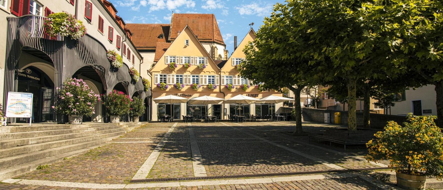 Marktplatz in Bietigheim-Bissingen mit historischen Gebäuden, Blumen und Sonnenschirmen vor einem Café. Ein Baum spendet Schatten., © Stuttgart Marketing GmbH, Sarah Schmid