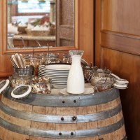 Ein Frühstücksbuffet auf einem Weinfass mit Milch, Nüssen, Besteck und Tellern in einem rustikalen Restaurant., © Badhotel Restaurant Stauferland