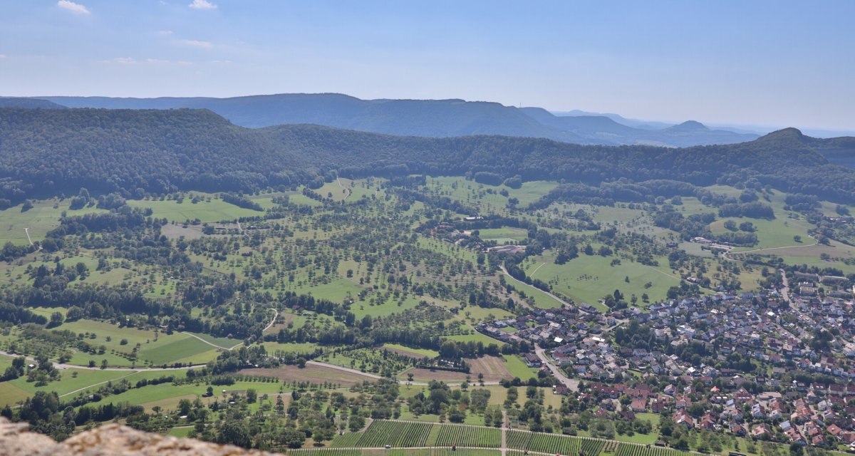 Panoramablick von der Burg Hohenneuffen über grüne Streuobstwiesen, Weinberge und die Stadt Neuffen im Tal., © hochgehberge Panoramablick von der Burg Hohenneuffen über grüne Streuobstwiesen, Weinberge und die Stadt Neuffen im Tal., © hochgehberge