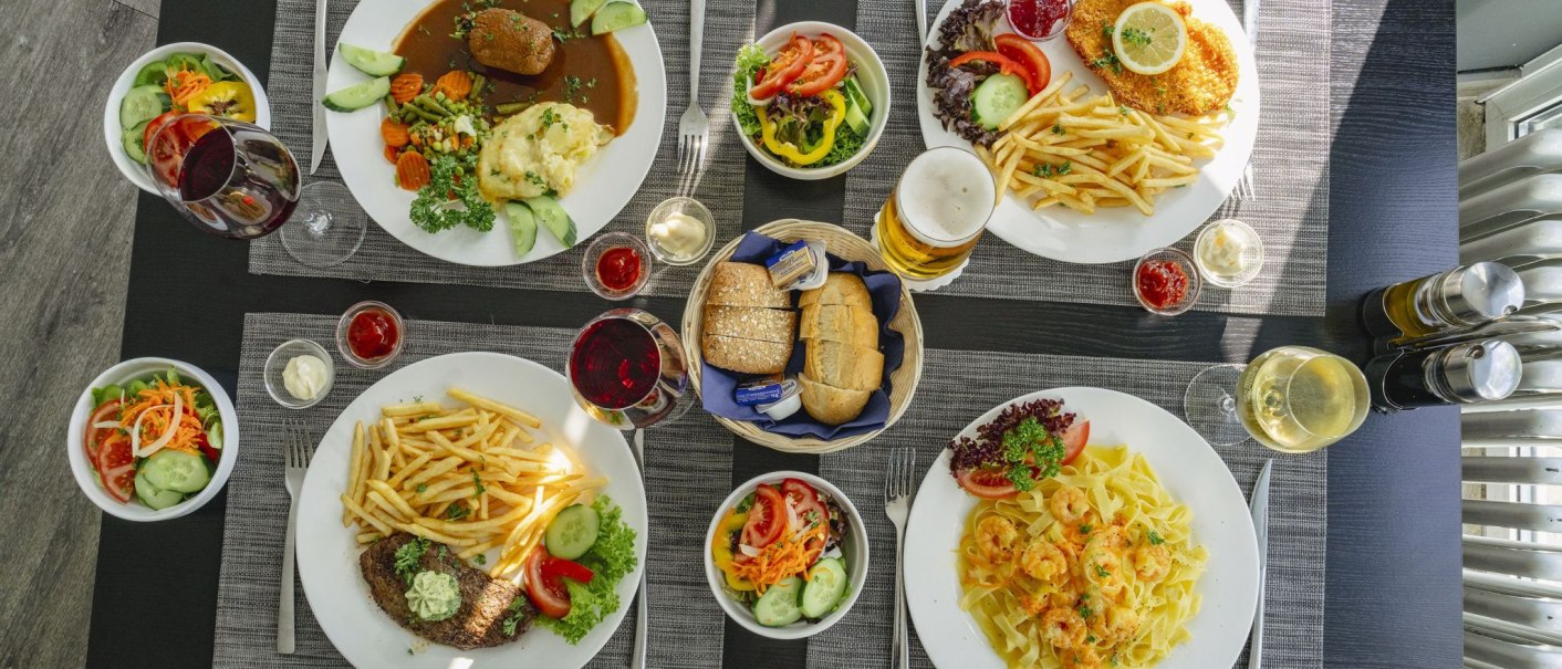 Ein Tisch mit verschiedenen Gerichten: Fleisch, Pommes, Salat, Pasta, Brot und Getränke wie Wein und Bier in einem Restaurant., © Plaza INN Stuttgart-Filderstadt Ein Tisch mit verschiedenen Gerichten: Fleisch, Pommes, Salat, Pasta, Brot und Getränke wie Wein und Bier in einem Restaurant., © Plaza INN Stuttgart-Filderstadt
