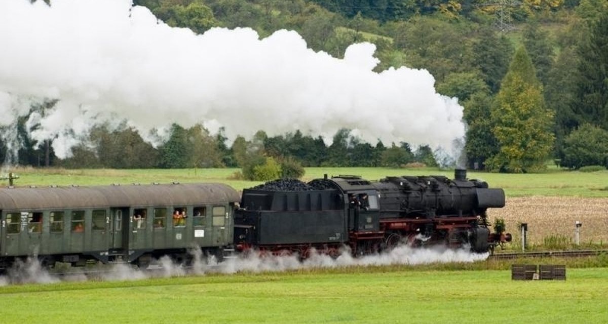 Eine historische Dampflok der Schw&auml;bischen Waldbahn zieht Waggons durch eine gr&uuml;ne Landschaft, umgeben von B&auml;umen und Feldern., &copy; Aktiv-Region Stuttgart
