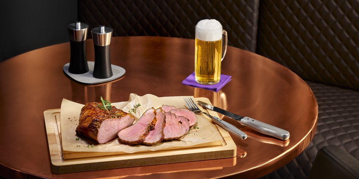 Ein Tisch mit geschnittenem Fleisch auf einem Holzbrett, Besteck, Salz- und Pfefferstreuer und einem Bierkrug., © Jaz Hotel Stuttgart