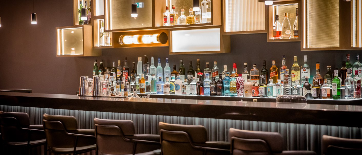 Elegante Bar mit stilvoller Beleuchtung, Flaschen und Gläsern auf der Theke. Moderne Hocker stehen bereit, die Atmosphäre ist gediegen und einladend., © TOMAS Elegante Bar mit stilvoller Beleuchtung, Flaschen und Gläsern auf der Theke. Moderne Hocker stehen bereit, die Atmosphäre ist gediegen und einladend., © TOMAS
