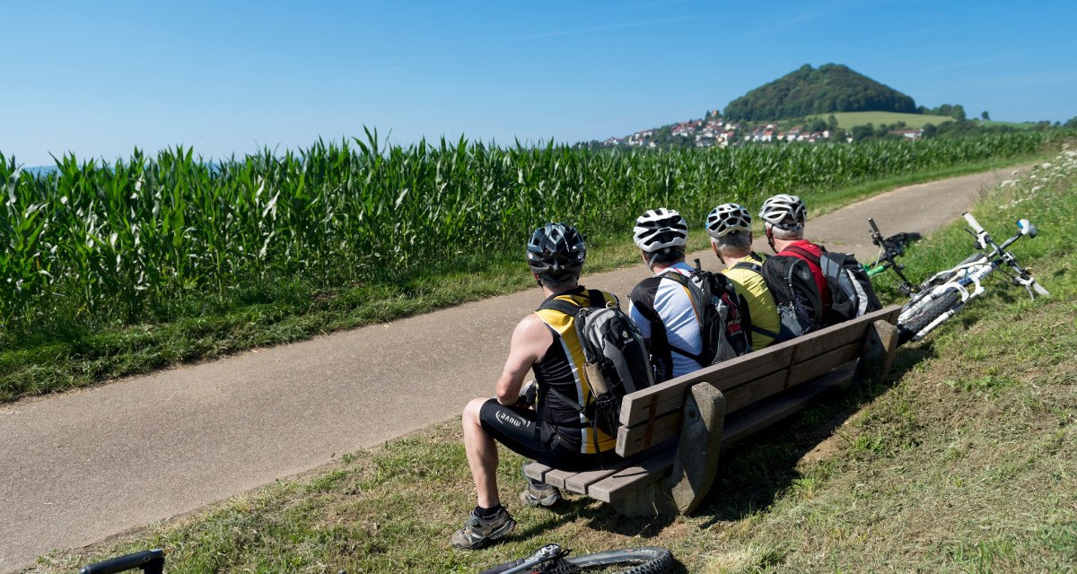 Drei Radfahrer mit Helmen sitzen auf einer Bank am Wegesrand, Fahrräder liegen daneben. Im Hintergrund ist der Hohenstaufen zu sehen., © Landkreis Göppingen Drei Radfahrer mit Helmen sitzen auf einer Bank am Wegesrand, Fahrräder liegen daneben. Im Hintergrund ist der Hohenstaufen zu sehen., © Landkreis Göppingen