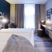 Modernes Zimmer mit Doppelbett, Schreibtisch, Flachbildfernseher und Dekoration. Schriftzug 'AHOI' an der Wand, neutrale Farben und gemütliche Atmosphäre., © HARBR. hotel Ludwigsburg / DQuadrat Living GmbH