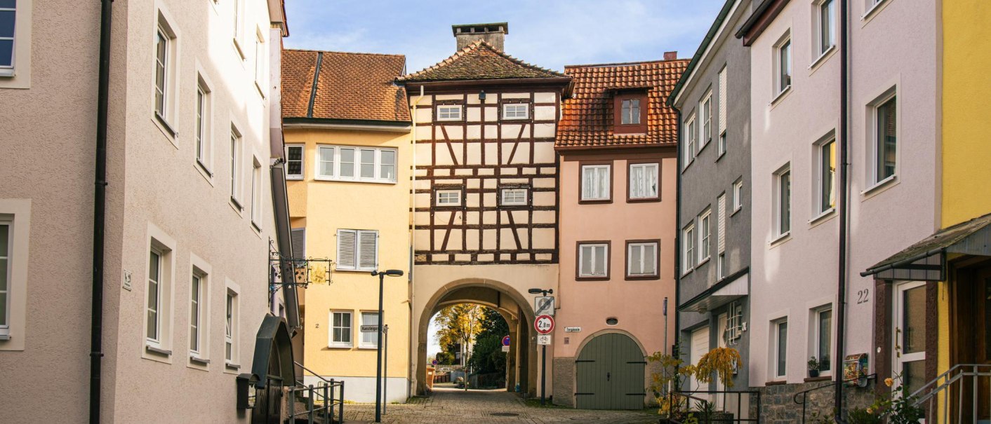 Fachwerkhaus in Künzelsau: Ein Torbogen führt durch ein traditionelles Fachwerkgebäude in einer engen Altstadtgasse., © Stuttgart-Marketing GmbH, Sarah Schmid