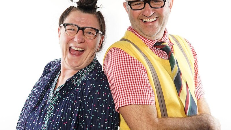 Zwei fröhliche Personen in bunter Kleidung stehen Rücken an Rücken und lachen in die Kamera., © NPG Messe und Veranstaltungs-GmbH