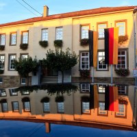 Das Rathaus in Waiblingen-Hohenacker, geschmückt mit Blumen und deutschen Flaggen, spiegelt sich auf einer glänzenden Oberfläche wider., © Waiblingen - Stuttgart-Marketing GmbH