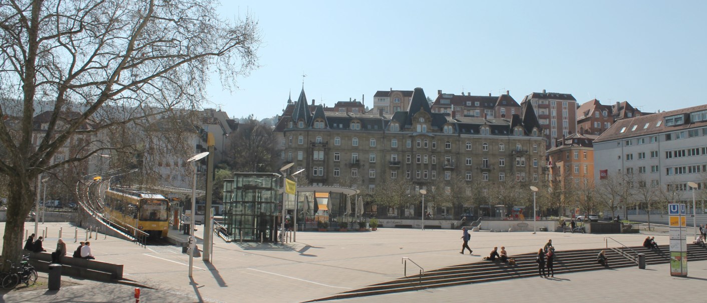 Marienplatz in Stuttgart mit Straßenbahn, modernen und historischen Gebäuden. Menschen sitzen auf Treppen, Bäume ohne Laub, sonniger Tag., © Stuttgart-Marketing GmbH Marienplatz in Stuttgart mit Straßenbahn, modernen und historischen Gebäuden. Menschen sitzen auf Treppen, Bäume ohne Laub, sonniger Tag., © Stuttgart-Marketing GmbH