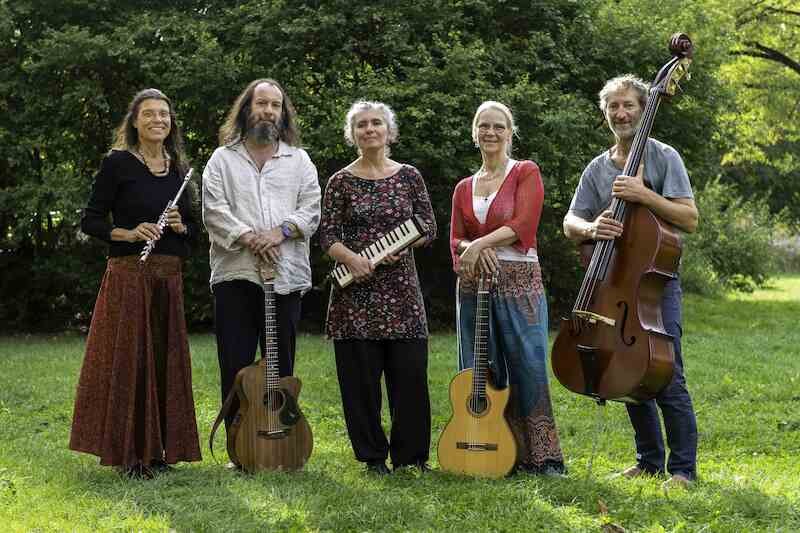 Fünf Personen stehen auf einer Wiese mit Instrumenten: Flöte, Gitarre, Melodica, Gitarre und Kontrabass. Im Hintergrund sind Bäume zu sehen., © Kulturhaus Schwanen