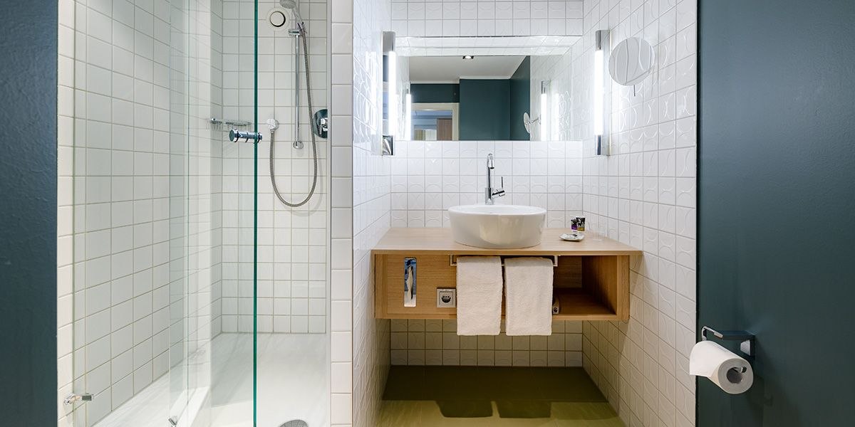 Modernes Badezimmer mit Glasdusche, weiß gefliest. Holzwaschtisch mit rundem Waschbecken, Spiegel und Beleuchtung., © Mercure Bristol Stuttgart Sindelfingen