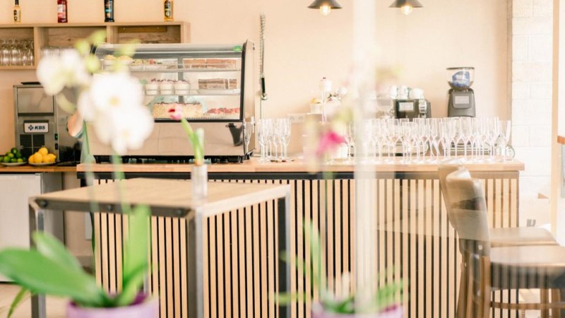 Ein stilvolles Caf&eacute; mit einer modernen Theke, Barhockern und Orchideen im Vordergrund. Im Hintergrund sind Gl&auml;ser und Flaschen zu sehen., &copy; Magnolia