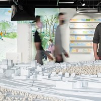 Ein Mann betrachtet ein Architekturmodell in einer Ausstellung. Im Hintergrund sind Illustrationen und Notizen an der Wand zu sehen., © Stadt Stuttgart / Dominique Brewing