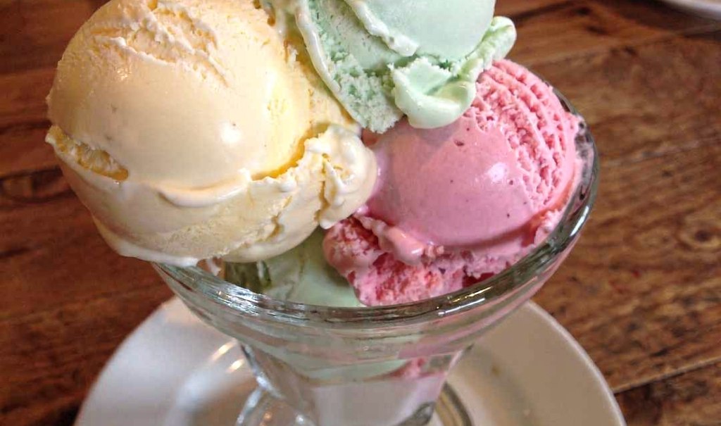 Ein Glasbecher mit drei Kugeln Eis in den Farben Gelb, Gr&uuml;n und Rosa steht auf einem Holztisch., &copy; StadtN&uuml;rtingen