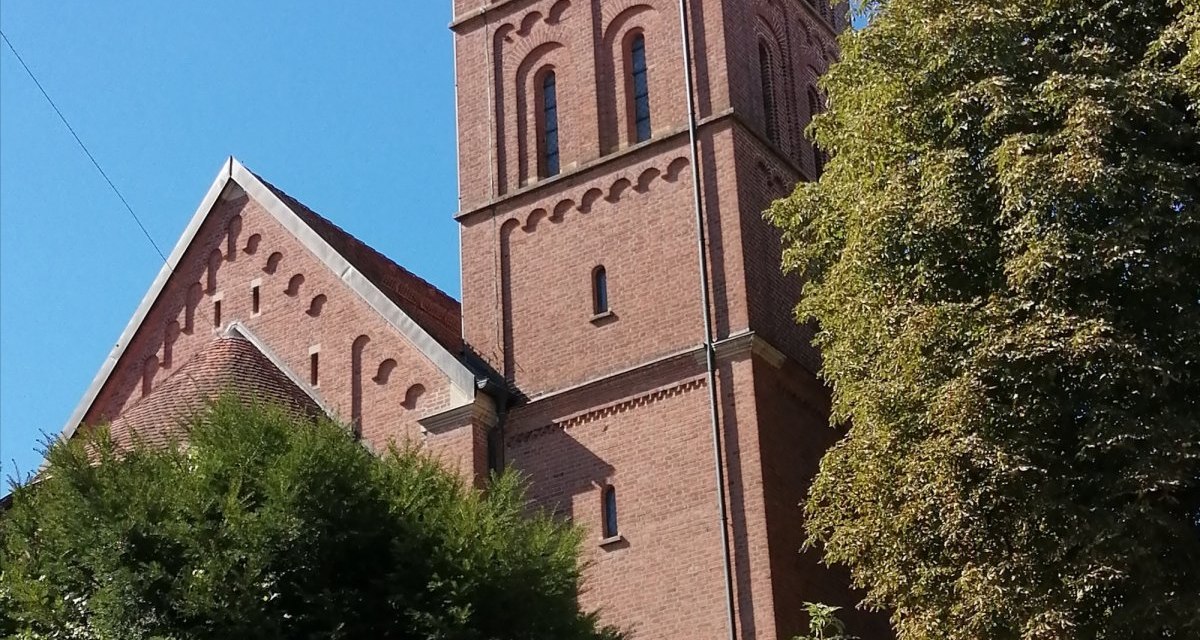 Die katholische Kirche St. Jakobus in Bargau mit ihrem markanten roten Backsteinturm und einer Uhr, umgeben von grünen Bäumen und strahlend blauem Himmel., © Foto: Cornelia Steinbach Die katholische Kirche St. Jakobus in Bargau mit ihrem markanten roten Backsteinturm und einer Uhr, umgeben von grünen Bäumen und strahlend blauem Himmel., © Foto: Cornelia Steinbach