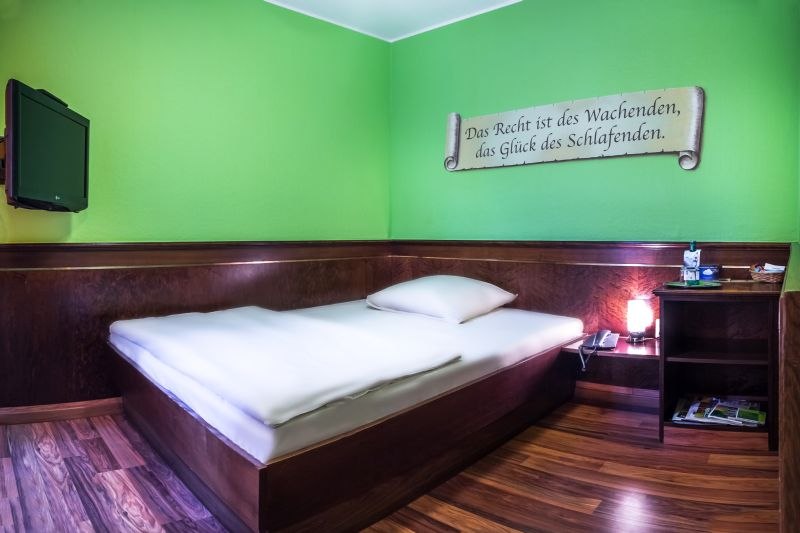 Zimmer mit grün gestrichenen Wänden, französischem Bett, Wandzitat und kleinem Nachttisch mit Lampe., © TOMAS