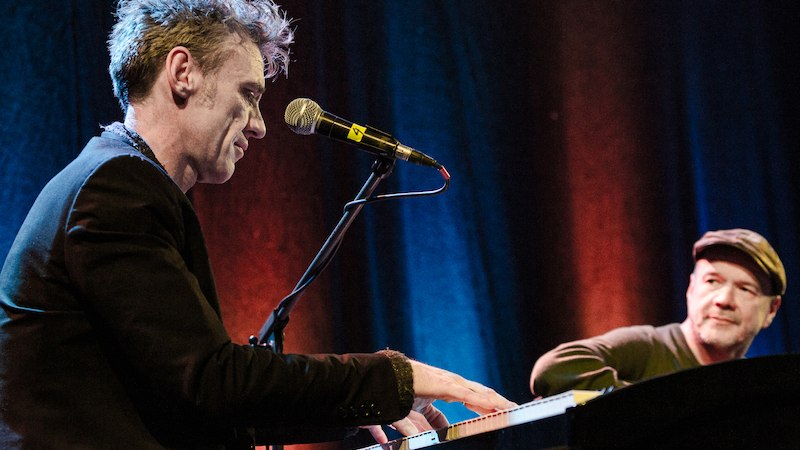 Zwei Musiker auf der B&uuml;hne, einer spielt Keyboard, w&auml;hrend der andere aufmerksam zuschaut. Die B&uuml;hne ist in warmen Farben beleuchtet., &copy; Kulturhaus Schwanen