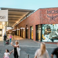 Einkaufsstra&szlig;e in der Outletcity Metzingen mit Gesch&auml;ften wie MCM. Menschen schlendern vorbei, einige sind in Bewegung unscharf., &copy; OUTLETCITY AG