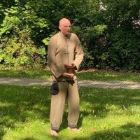 Ein Mann in traditioneller Qigong-Kleidung steht barfu&szlig; auf einer Wiese und f&uuml;hrt eine &Uuml;bung durch. Im Hintergrund sind B&auml;ume und B&uuml;sche zu sehen., &copy; Daniel Steinbauer
