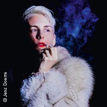 Person mit blondem Haar und Pelzmantel raucht, blauer Rauch im Hintergrund. Dunkler Hintergrund, dramatische Beleuchtung., &copy; links im Bild