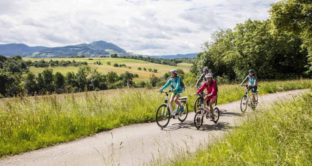 Eine Familie fährt auf einem Radweg durch eine grüne Landschaft mit Hügeln im Hintergrund. Der Himmel ist bewölkt., © Schwäbische Alb Tourismusverband e.V. Eine Familie fährt auf einem Radweg durch eine grüne Landschaft mit Hügeln im Hintergrund. Der Himmel ist bewölkt., © Schwäbische Alb Tourismusverband e.V.