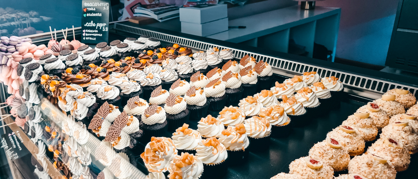 Eine Vitrine voller bunter Cupcakes und Macarons, kunstvoll dekoriert mit Sahne und Schokolade., &copy; Cupcakes & Bagels, Stuttgart