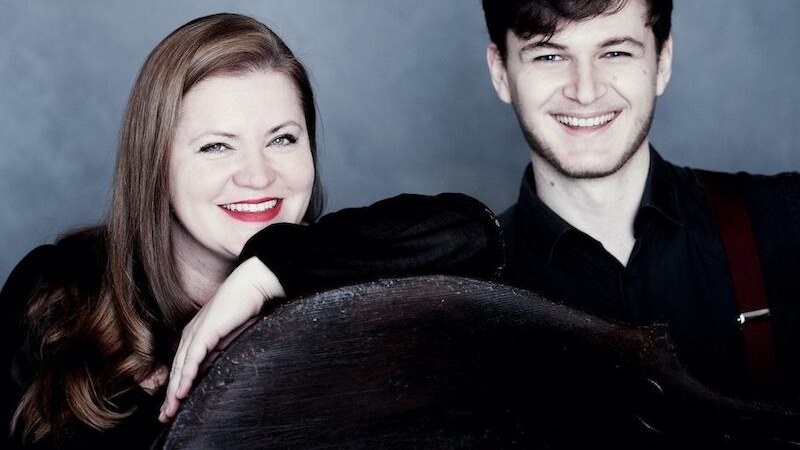 Zwei Personen lächeln in die Kamera, eine Frau lehnt sich auf einen Kontrabass. Der Hintergrund ist grau., © Kammerkonzerte Schwäbisch Hall e.V.