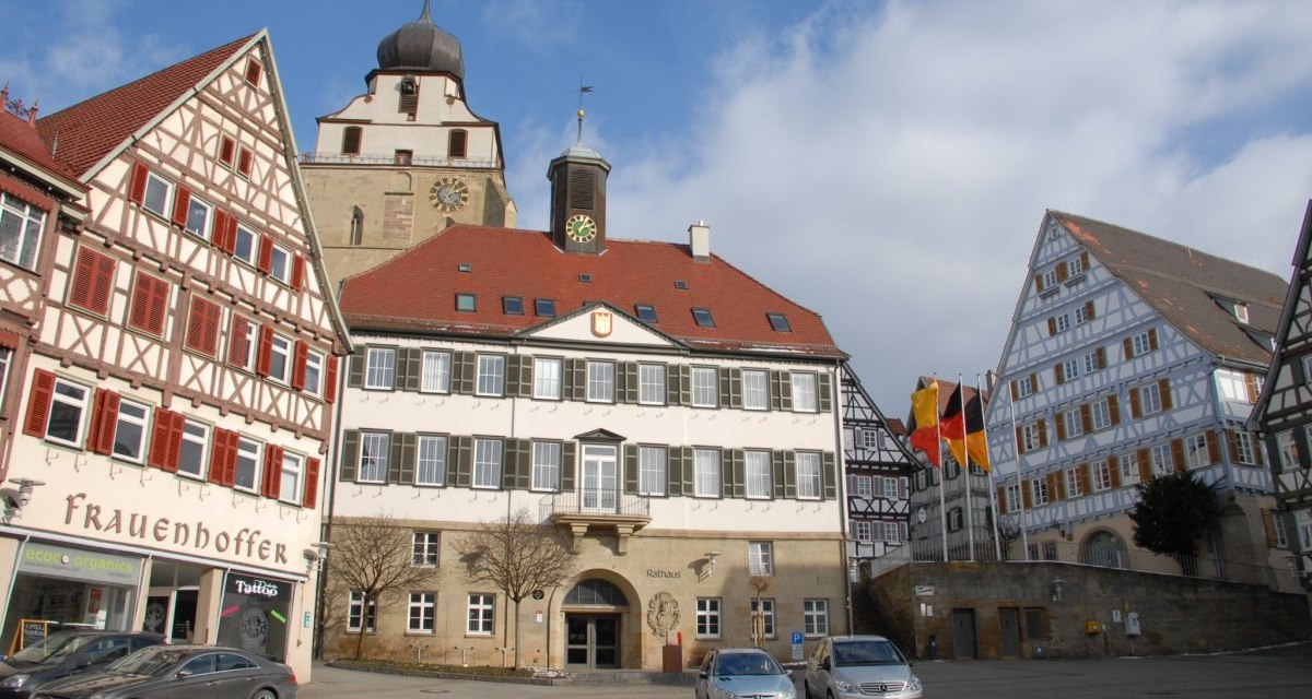 Der Marktplatz in Herrenberg zeigt Fachwerkhäuser und das Rathaus unter blauem Himmel. Autos parken vor den Gebäuden., © Natur.Nah. Schönbuch & Heckengäu Der Marktplatz in Herrenberg zeigt Fachwerkhäuser und das Rathaus unter blauem Himmel. Autos parken vor den Gebäuden., © Natur.Nah. Schönbuch & Heckengäu