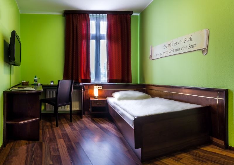 Ein gem&uuml;tliches Einzelzimmer mit gr&uuml;n gestrichenen W&auml;nden, einem Einzelbett, Schreibtisch und Stuhl. Ein roter Vorhang h&auml;ngt am Fenster., &copy; TOMAS