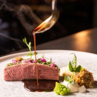 Ein kunstvoll angerichtetes Gourmetgericht mit Fleisch, Gemüse und einer dunklen Sauce, die aus einer Kelle auf den Teller gegossen wird., © 5 - Stuttgart