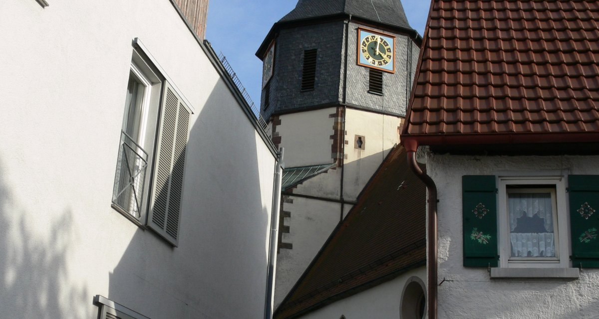 Spitzer Kirchturm der evangelischen Pfarrkirche St. Clemens ragt zwischen weißen Wohnhäusern hervor, blauer Himmel im Hintergrund., © Land der 1000 Hügel - Kraichgau-Stromberg Spitzer Kirchturm der evangelischen Pfarrkirche St. Clemens ragt zwischen weißen Wohnhäusern hervor, blauer Himmel im Hintergrund., © Land der 1000 Hügel - Kraichgau-Stromberg